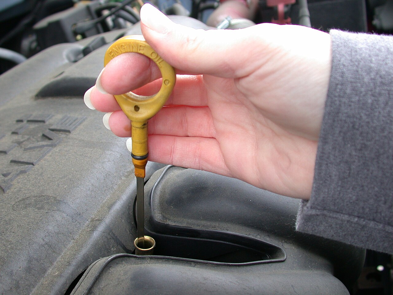 Motor yağ çubuğunu kontrol eden bir el ve motor bloğu